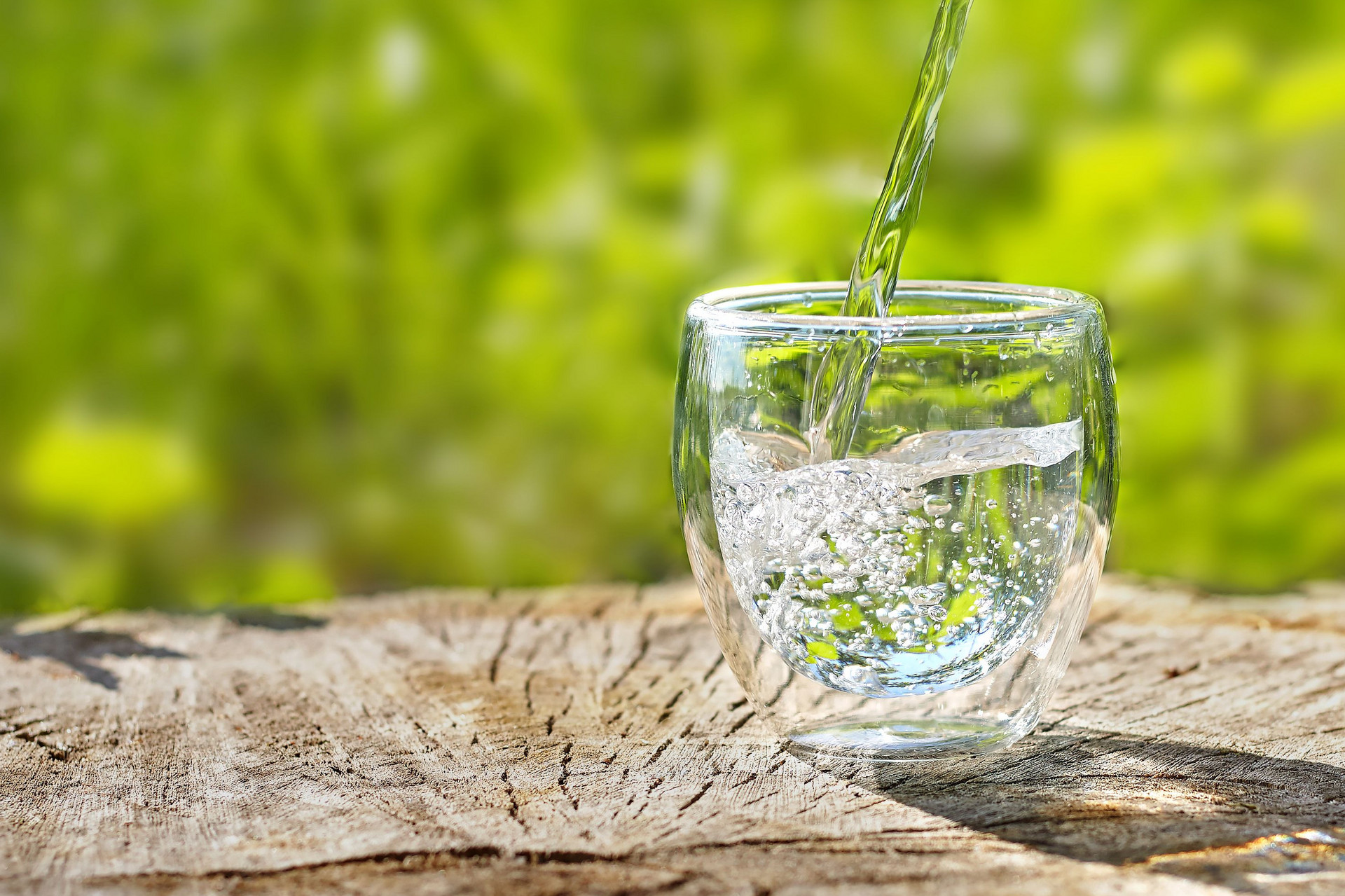 Wasser wird vor einem grünen Hintergrund in ein Glas gegossen 